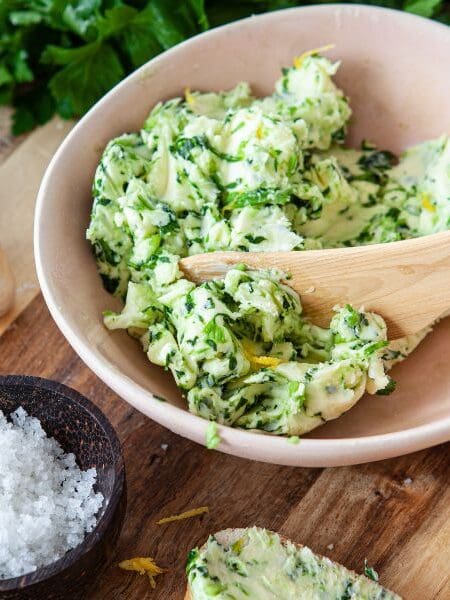 Kräuterbutter Rezept - Schale mit angerührter Kräuterbutter, daneben Knoblauch, Salz, Petersilie und Brot