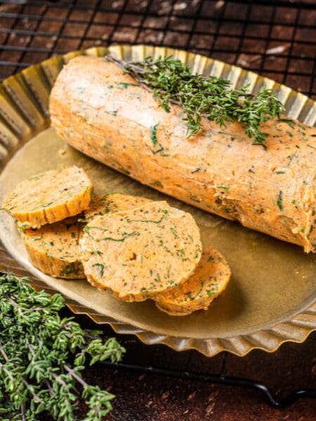Tomatenbutter Rezept, rund geformte Tomatenbutter in einer goldenen Servierschale mit Kräutern als Dekoration