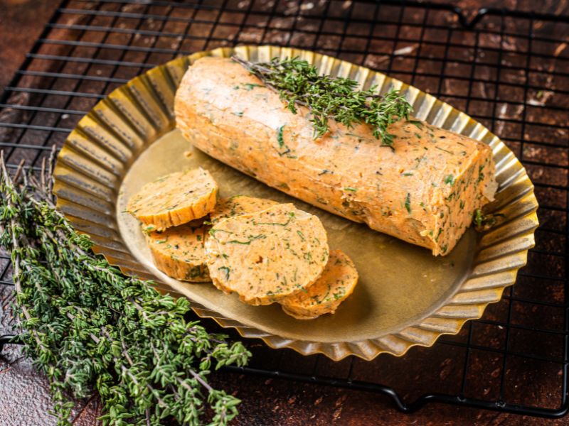 Tomatenbutter Rezept, rund geformte Tomatenbutter in einer goldenen Servierschale mit Kräutern als Dekoration